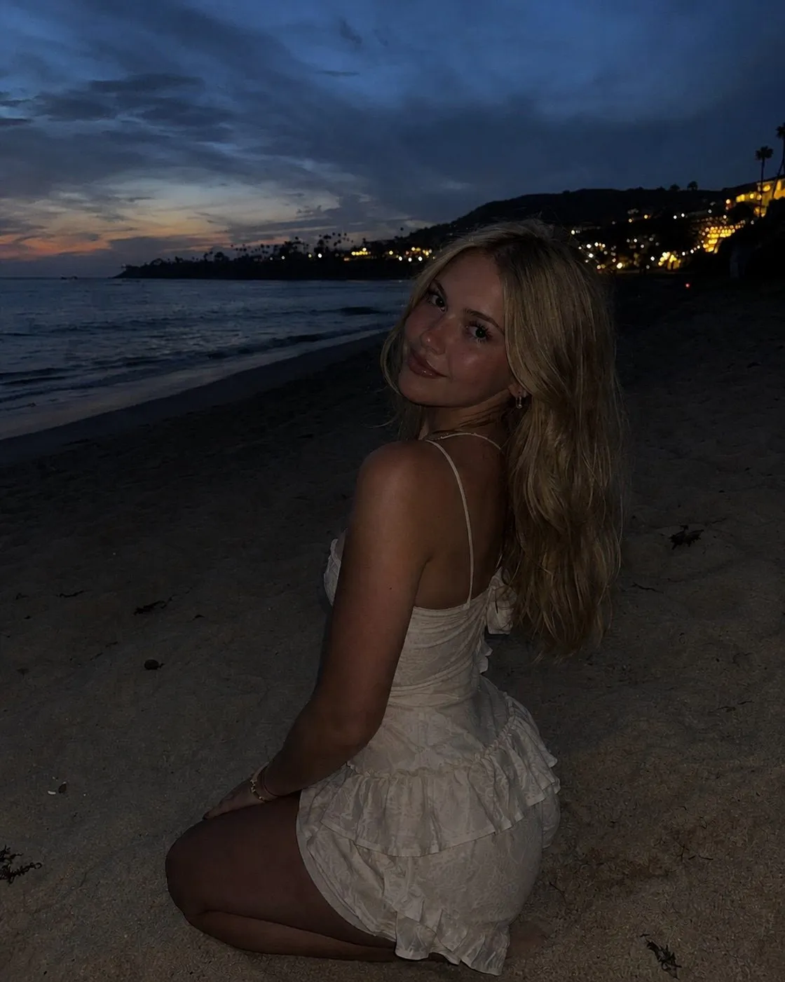 A woman kneeling on a beach at dusk, the photo so dark her face is hard to see